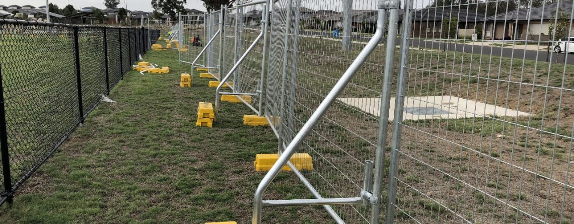Temporary fencing with bracing bars and yellow stabiliser blocks installed on grassy site in suburban Australia