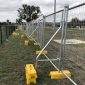Temporary fencing with bracing bars and yellow stabiliser blocks installed on grassy site in suburban Australia